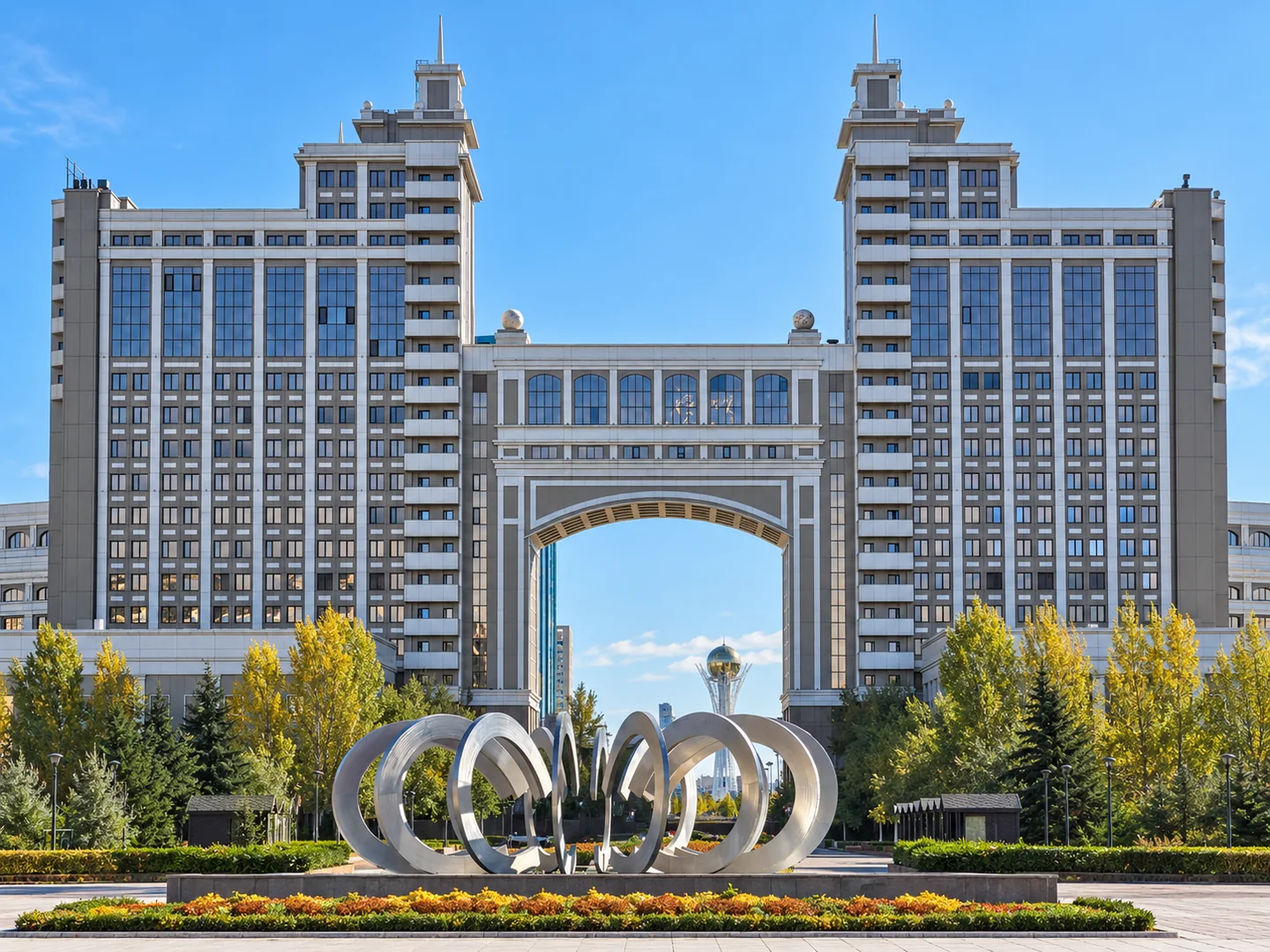 A gateway connecting two towers, with a circular sculpture in the foreground.