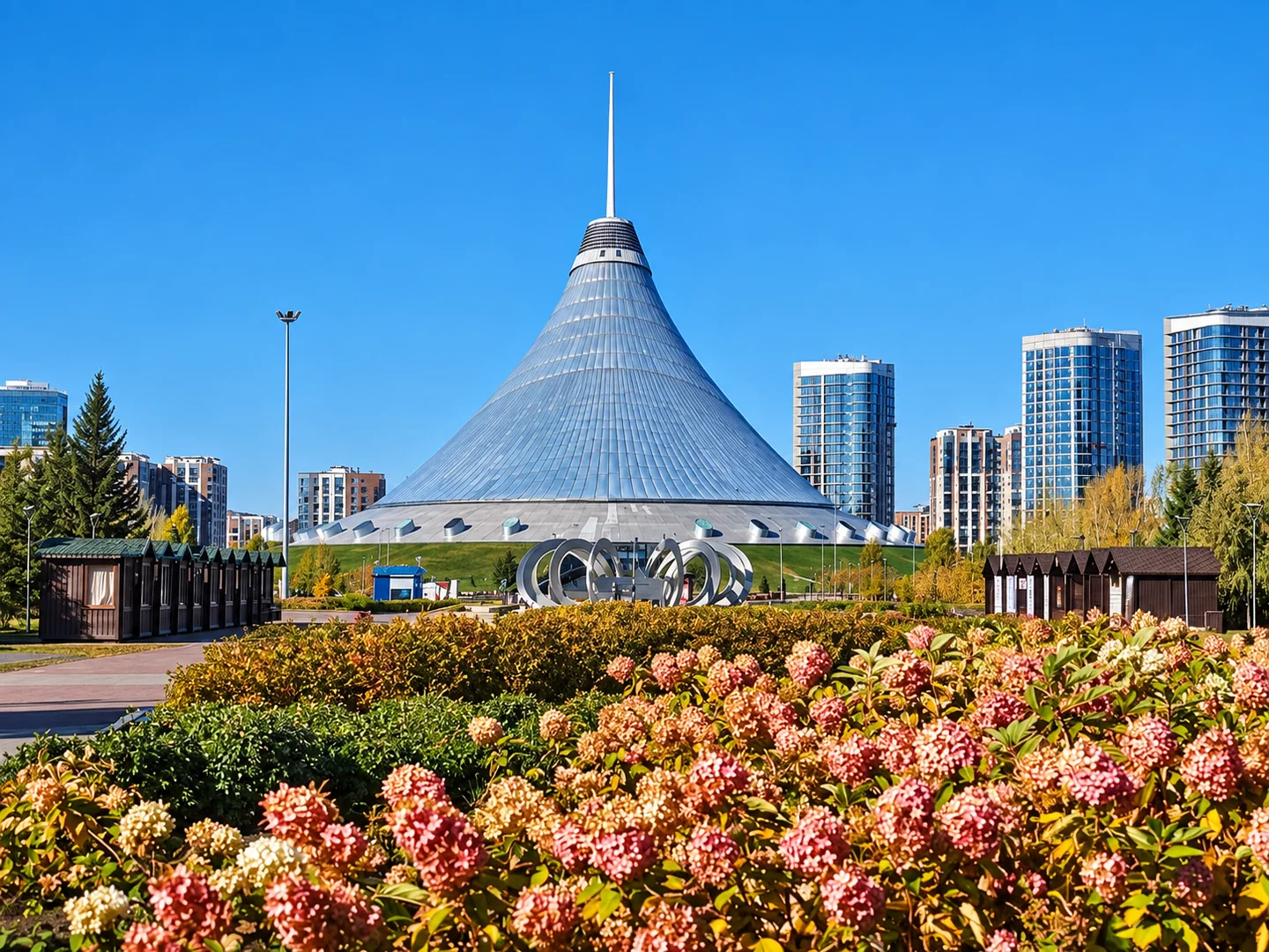 A tent-shaped building with a tall spire, landscaped gardens and a circular sculpture.